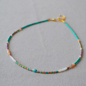 Detail of colorful turquoise and lavender beads with a gold clasp on a gray surface