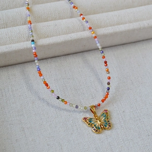 Détail du pendentif papillon doré émaillé avec collier de perles facettées colorées