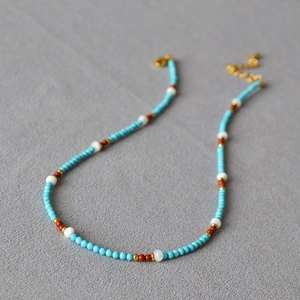 Close-up of bohemian beaded necklace with turquoise and pearls on grey textured background