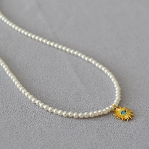 Détail d'un collier de perles blanches avec pendentif soleil doré et pierre turquoise