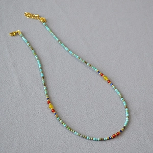 Detail view of handmade beaded necklace with turquoise and agate stones on grey fabric