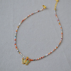 Détail d'un collier de perles fait main avec zircon coloré et pendentif papillon émaillé