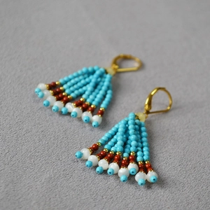 Gros plan de boucles d'oreilles bohèmes avec perles turquoise et pompons sur tissu gris
