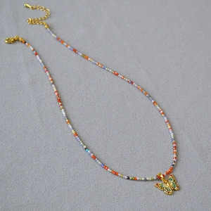 Détail macro du collier de perles colorées avec pendentif papillon émaillé et gemmes