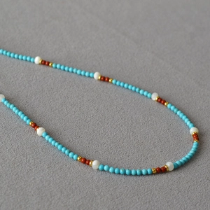 Detailed close-up of small turquoise and seashell beaded necklace with gold spacers