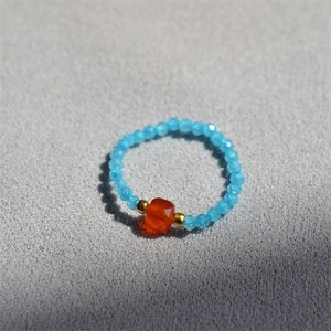 Detail of handmade beaded ring with light blue crystals and center orange bead accent