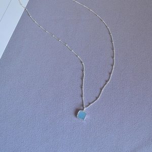 Close-up of light blue square gemstone pendant on a silver chain with hand-set edging