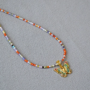 Détail du collier de perles avec pendentif papillon en émail bleu et gemmes colorées