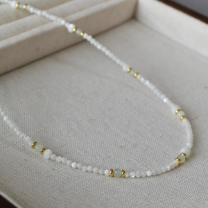 Macro shot of turquoise beads and white mother-of-pearl beads with gold accents on a necklace