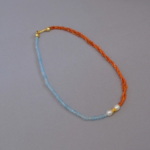 Detail of beaded necklace with blue faceted stones, orange beads, and white pearls