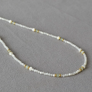 Macro detail of bead necklace with white shell pearls, green jade accents, and gold spacers