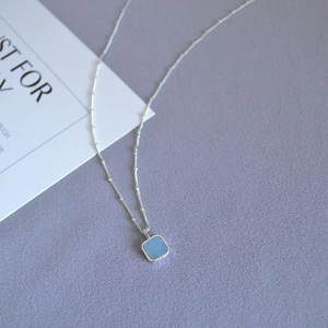 Detail view of square sky blue gemstone pendant on a silver beaded chain necklace