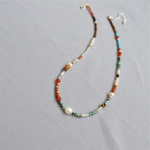 Collier de style ethnique avec perles colorées et perles d'eau douce sur un fond gris texturé