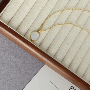 Detail einer minimalistischen Goldkette mit weißem Perlmutt-Anhänger und Blumenmuster