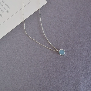 Detailed close-up of a silver beaded chain with a square pale blue gemstone pendant