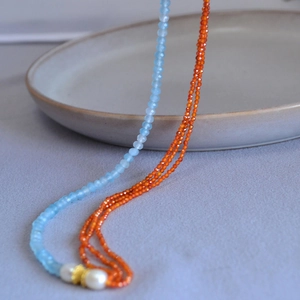 Blue and orange faceted bead necklace with white pearls and gold metal spacers on ceramic tray