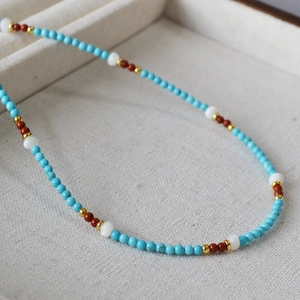 Macro detail of minimalist turquoise beaded necklace with red, white and gold accents