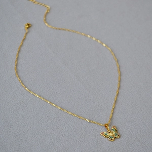 Détail de collier papillon doré avec émail bleu et strass colorés sur une chaîne fine