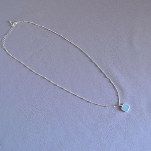 Macro shot of silver fine chain with square sky blue gemstone pendant on fabric