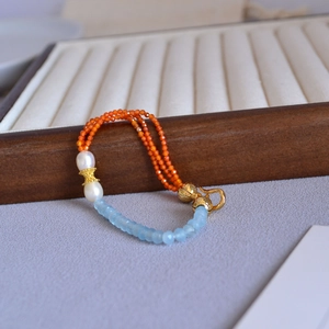 Detail of orange and blue faceted stone beads with pearls on a wooden jewelry stand