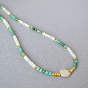 Close-up of handmade necklace with turquoise beads, white pearls, and golden spacers