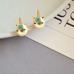 Cute enamel unicorn donut earrings with gold horn and floral detail on ceramic plate