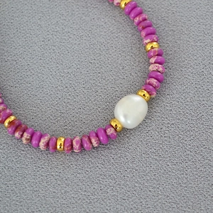 Close-up of lilac stone beads with a large baroque pearl and gold spacers on fabric
