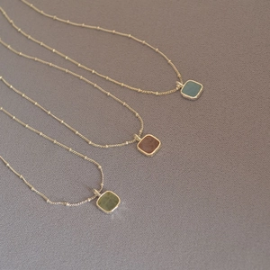 Close-up of geometric square aquamarine pendants on gold bead chains in three colors