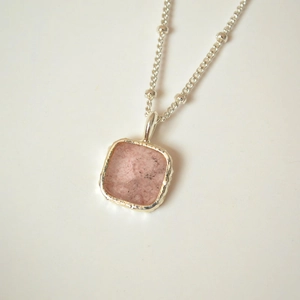 Detail of square pink gemstone pendant with silver bead chain showing natural mineral textures