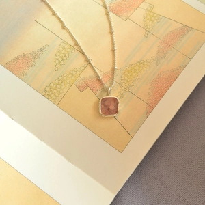 Macro shot of geometric square pink crystal pendant on a silver beaded chain necklace