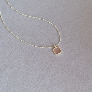 Close-up of geometric square aquamarine pendant with silver handmade edges on textured cloth