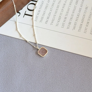 Detail view of square pink stone pendant with silver beaded chain on textured fabric