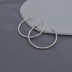 Macro shot of polished silver geometric C-shaped hoop earrings with butterfly backings