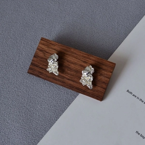 Macro shot of silver irregular lava texture earrings on a walnut wood stand