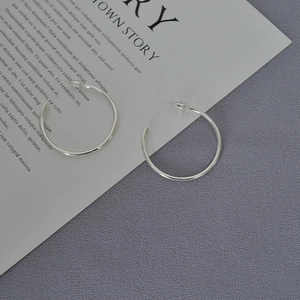 Close-up of polished silver hoop earrings on a textured gray and white aesthetic background