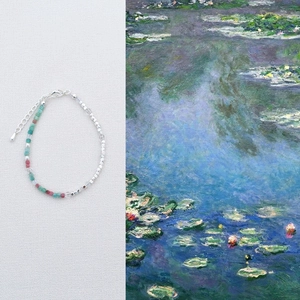 Artistic beaded necklace with green and red gemstones next to Monet oil painting