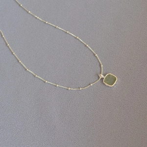 Macro shot of geometric square green gemstone pendant on silver beaded chain necklace
