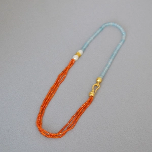 Detail of multi-strand orange beaded necklace with blue stones and a white pearl