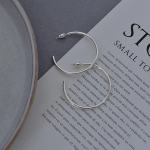 Macro shot of minimalist polished silver C-shaped hoop earrings on a textured plate