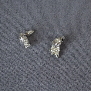 Macro shot of silver irregular lava texture earrings on dark textured fabric background