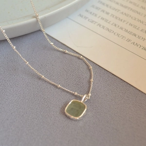Macro detail of geometric silver necklace with light green gemstone on purple fabric