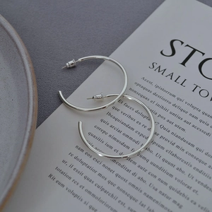Close-up of minimalist silver-plated C-shaped hoop earrings on a decorative paper card