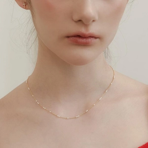Détail d'un collier chaîne dorée minimaliste avec petites perles blanches