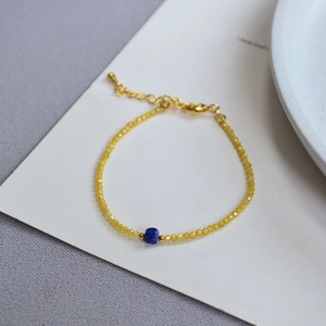 Macro view of faceted yellow beads and square blue stone on gold chain bracelet