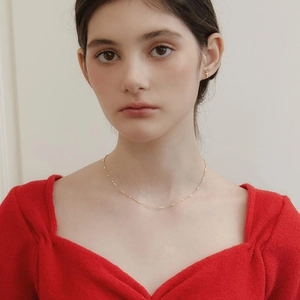 Détail du collier minimaliste en laiton doré avec petites perles et boucles croix