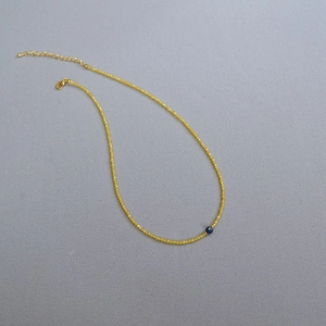Macro view of dainty yellow faceted bead necklace with a blue gemstone focal point