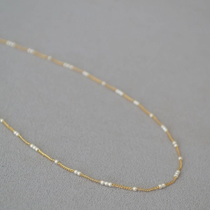 Détail d'un élégant collier en laiton doré orné de délicates mini perles blanches