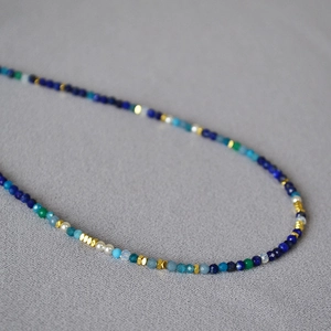 Artistic beaded necklace with blue lapis lazuli and gold accents on gray fabric