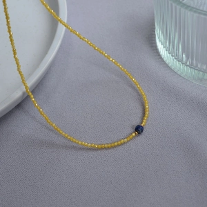 Detail of beaded necklace with yellow faceted beads and a blue gemstone centerpiece