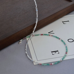 Detail of beaded necklace with silver cut beads, green stones, and pearls on a wooden tray